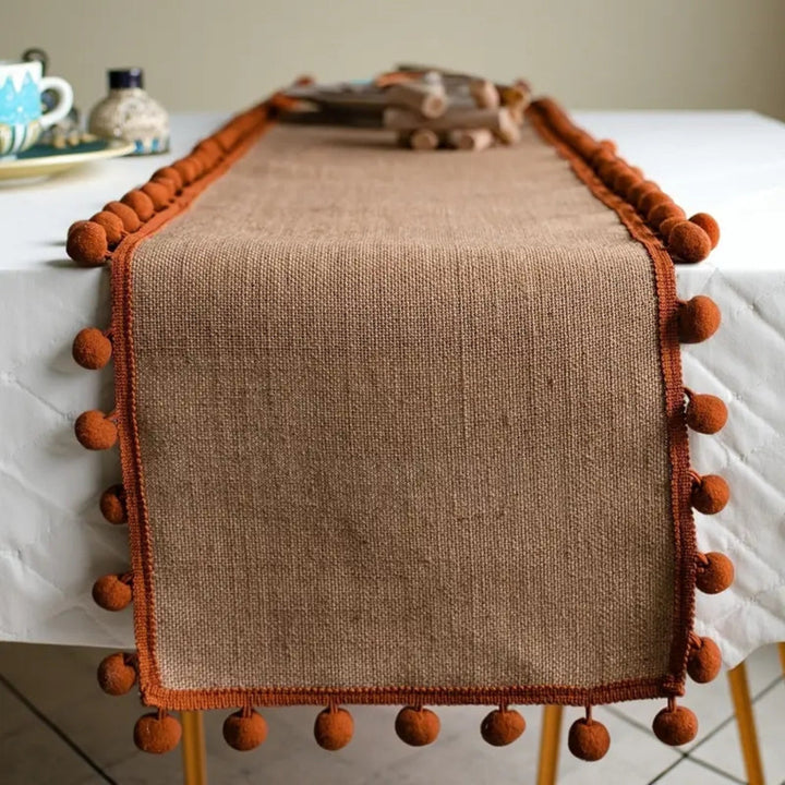 Jute-Tischläufer mit orangefarbenen Pompons