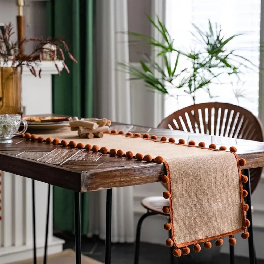Jute-Tischläufer mit orangefarbenen Pompons